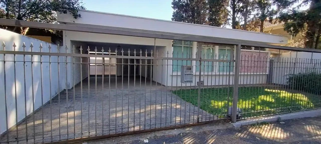 Vista frontal da casa com portão de metal, área de garagem e jardim gramado.