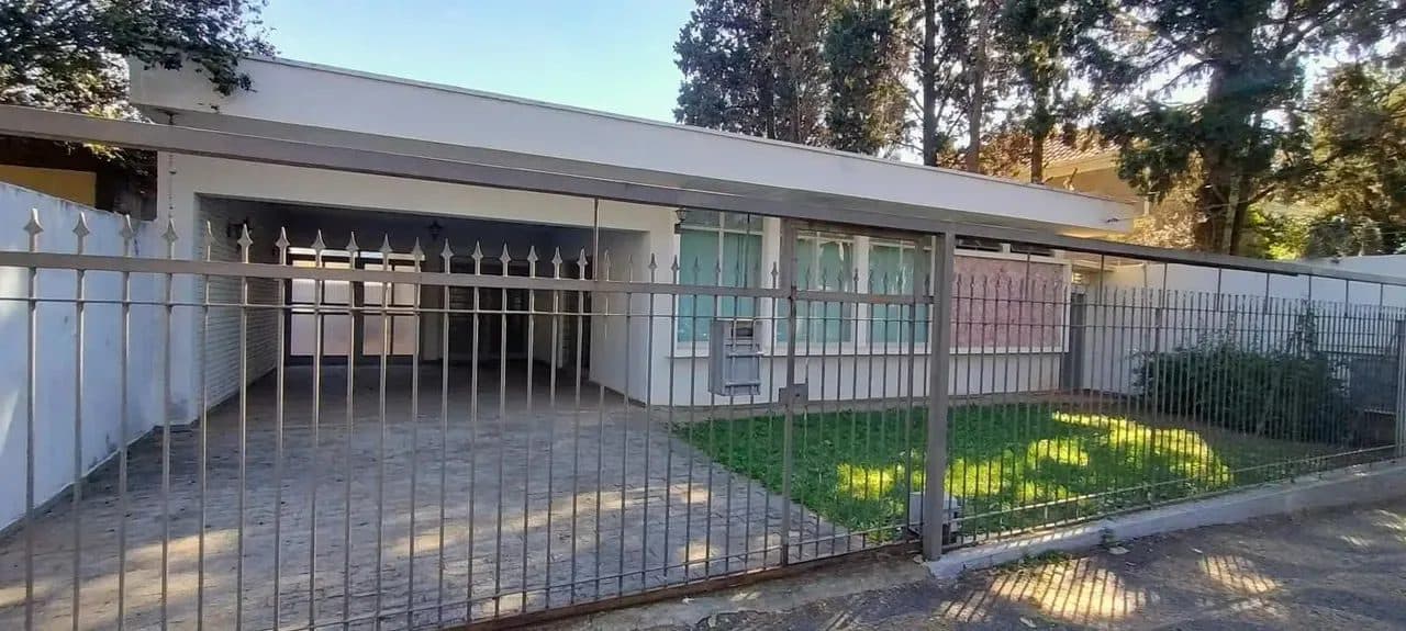 Fachada externa da residência com portão, garagem e jardim frontal.