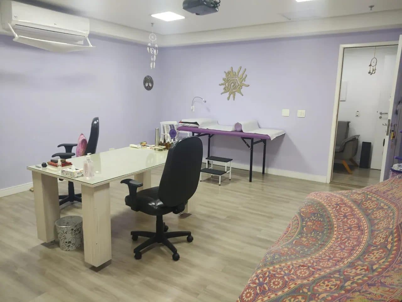 Sala comercial ampla com paredes roxas, mesa de escritório e maca