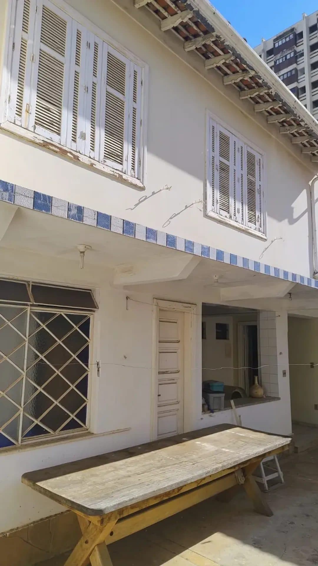 Fachada externa da casa com paredes brancas, janelas com venezianas de madeira e detalhes em azulejo azul.