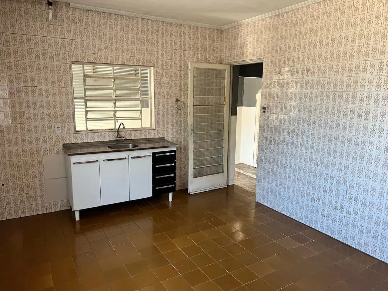 Cozinha com paredes totalmente revestidas com azulejos decorados, piso cerâmico marrom e balcão branco com pia