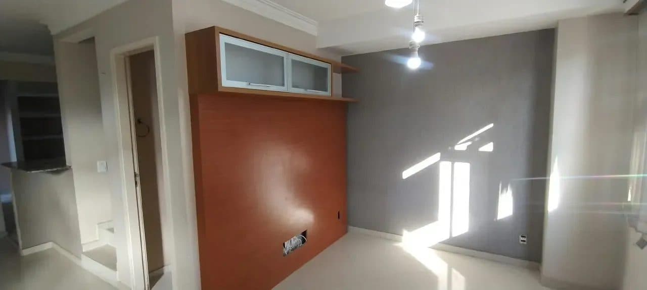 Sala com painel de TV em tom amadeirado e parede com acabamento em textura cinza.