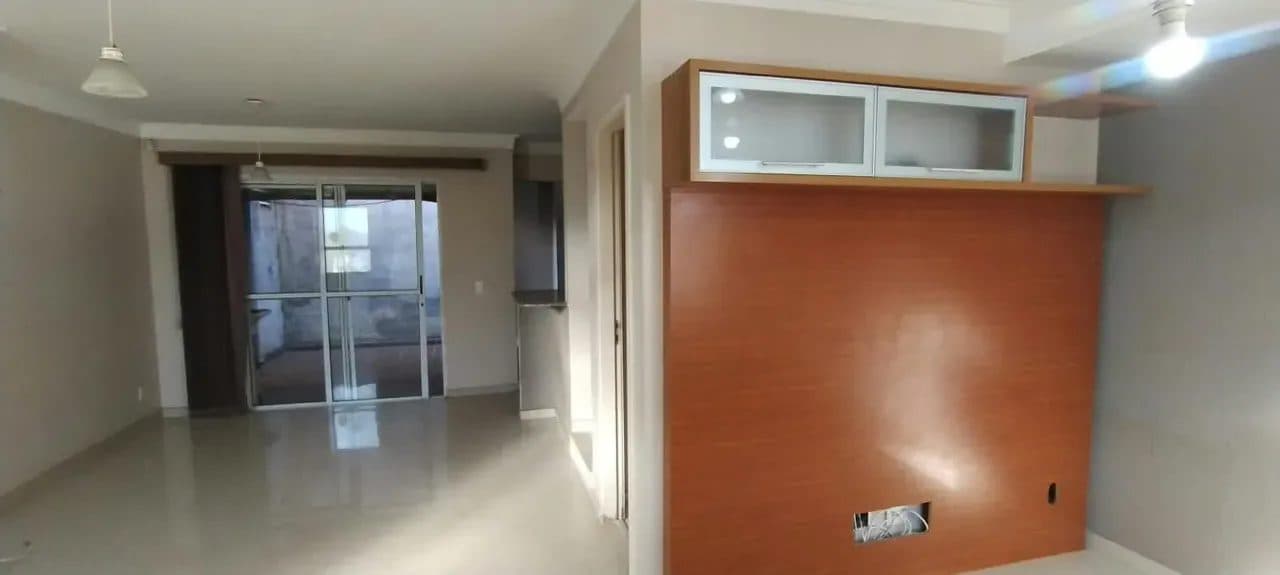 Sala de estar com painel de TV amadeirado e porta de correr de vidro com acesso à área externa.