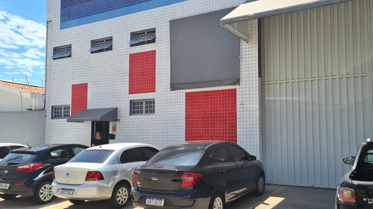 Fachada de galpão comercial com revestimento em pastilhas brancas, detalhes em vermelho e portão de correr metálico.