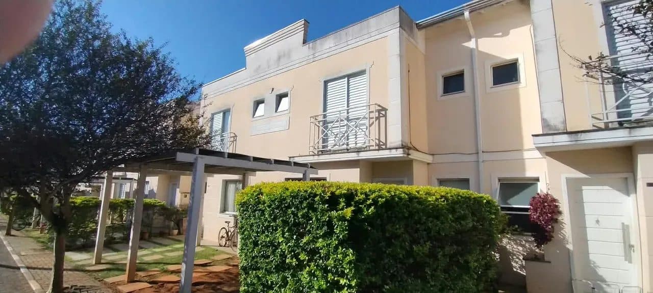 Fachada de casa em condomínio com pintura clara, sacada com guarda-corpo de ferro e jardim frontal.