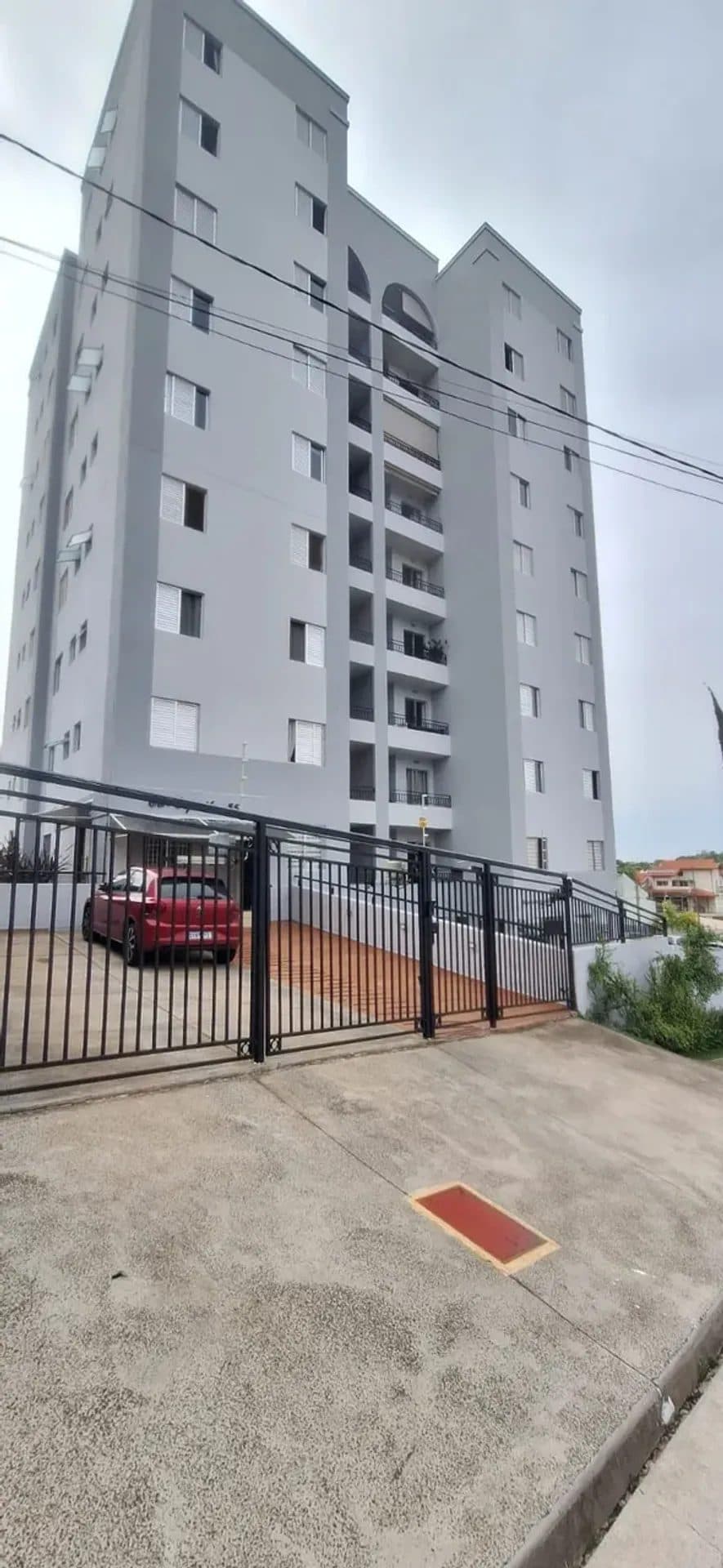 Fachada externa de edifício residencial cinza com portão de ferro e carro estacionado.