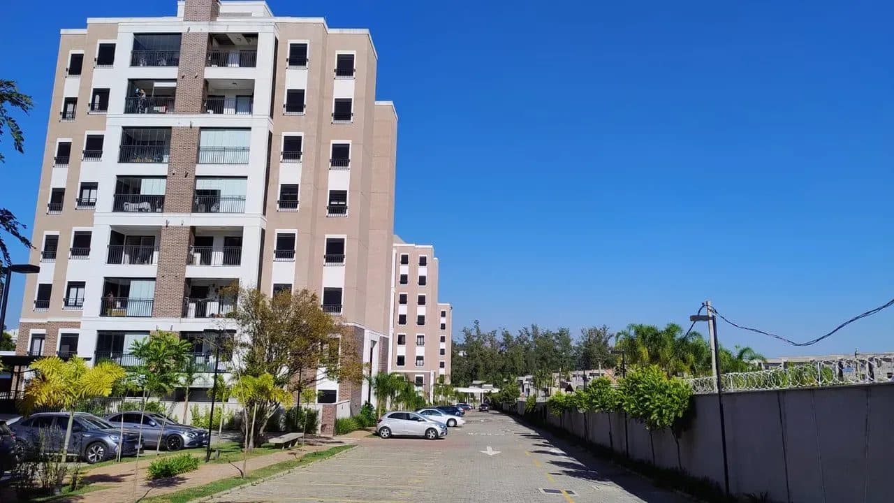 Vista externa do condomínio com prédios, estacionamento e área arborizada.