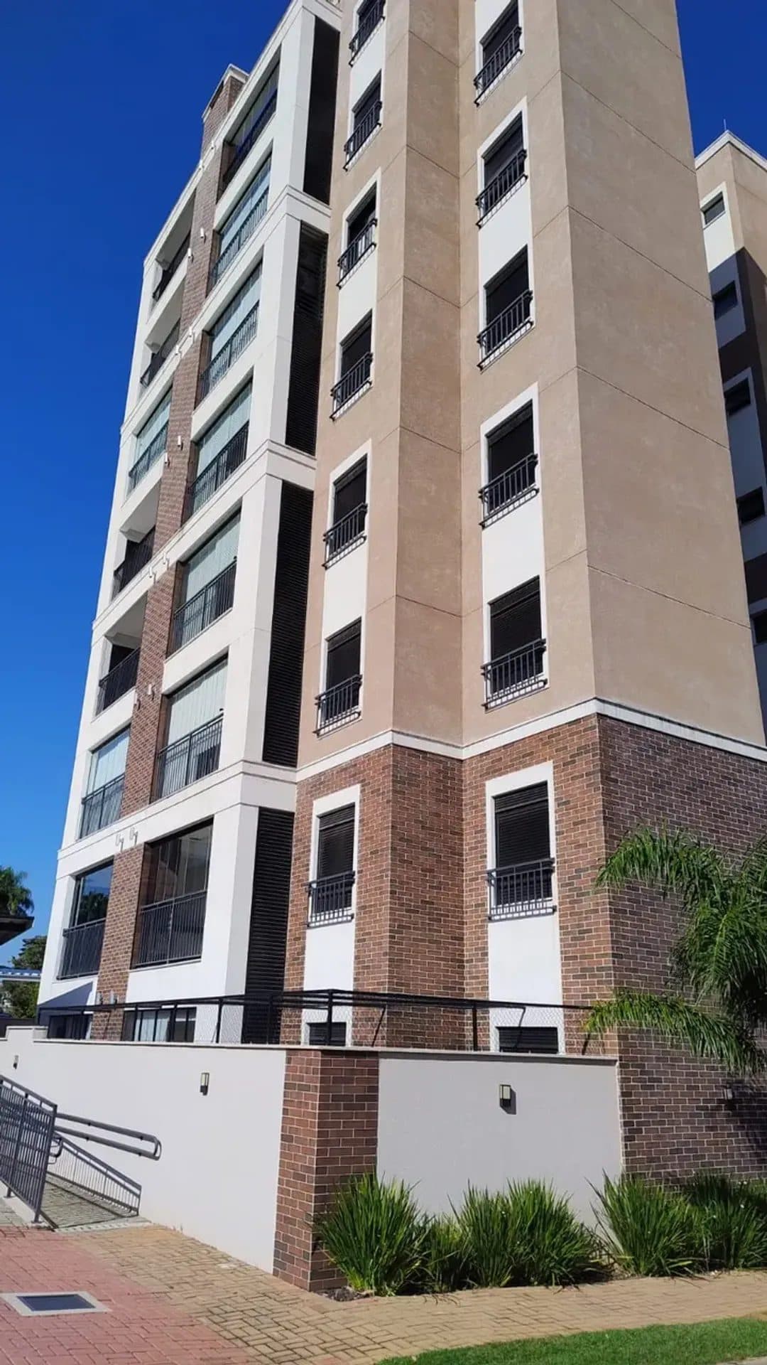 Fachada lateral de prédio residencial com varandas e acabamento em tijolinho.