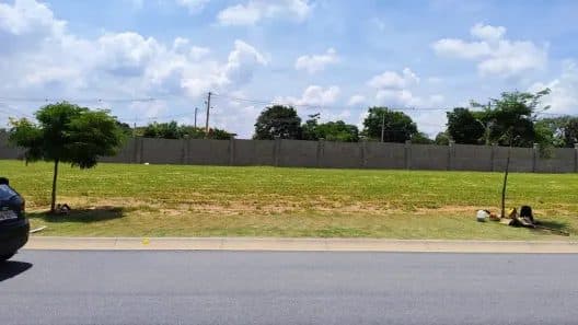 Terreno plano com gramado, cercado por muro de concreto e vista para a rua.