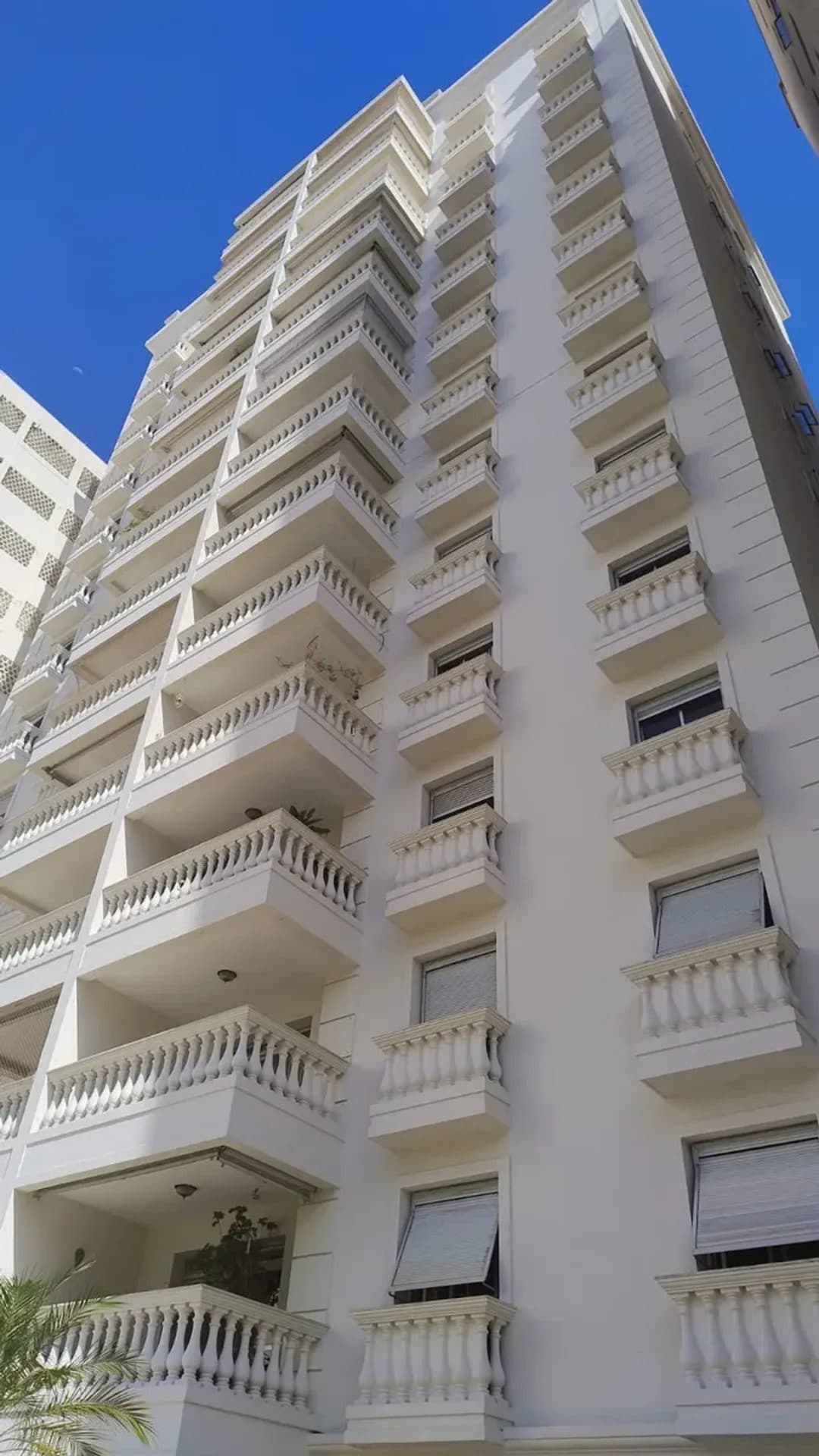 Fachada de prédio residencial branco com várias varandas com balaustradas.