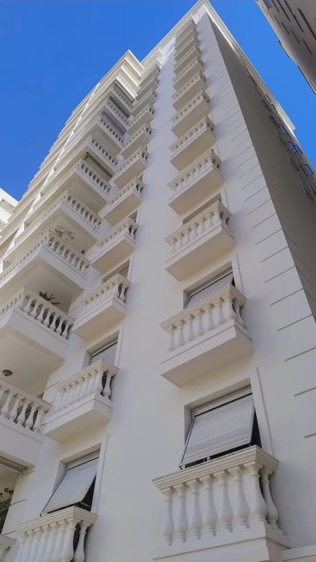 Detalhe da fachada do edifício residencial com sacadas e janelas em tom branco.