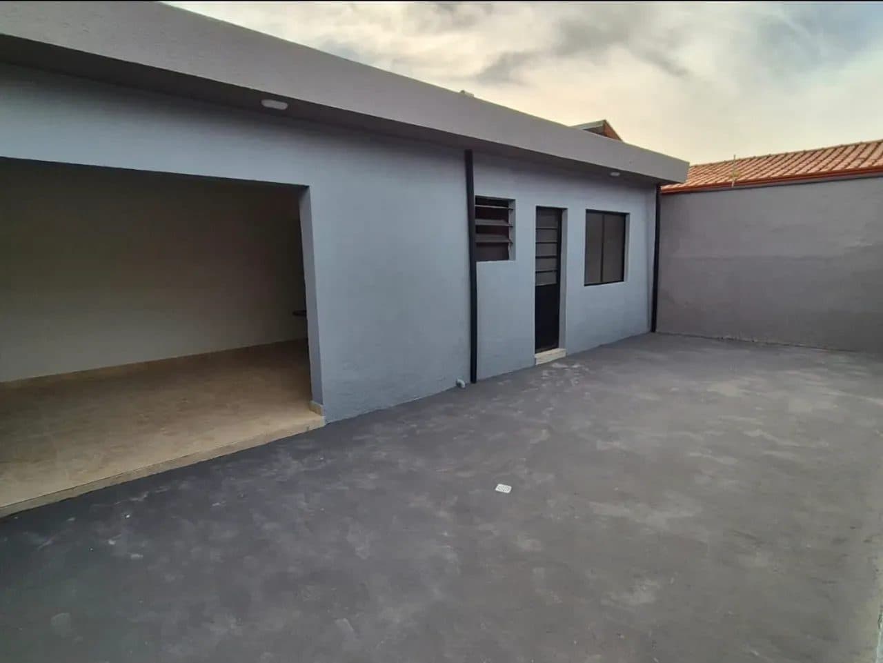 Área externa lateral da casa com piso de cimento cinza e paredes na mesma cor.