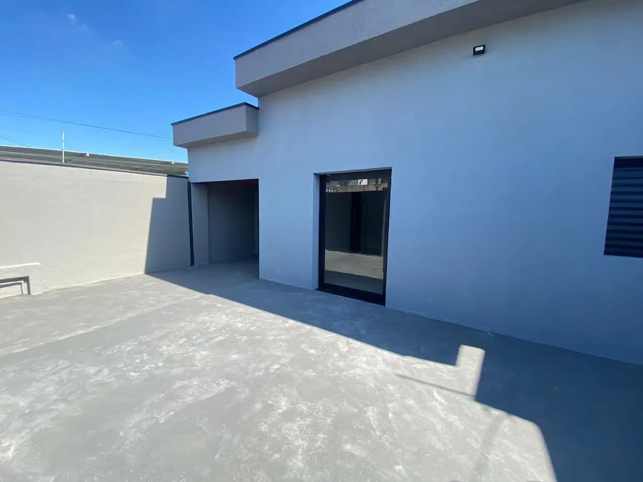 Área externa com piso cinza, fachada da casa e porta de vidro de correr.