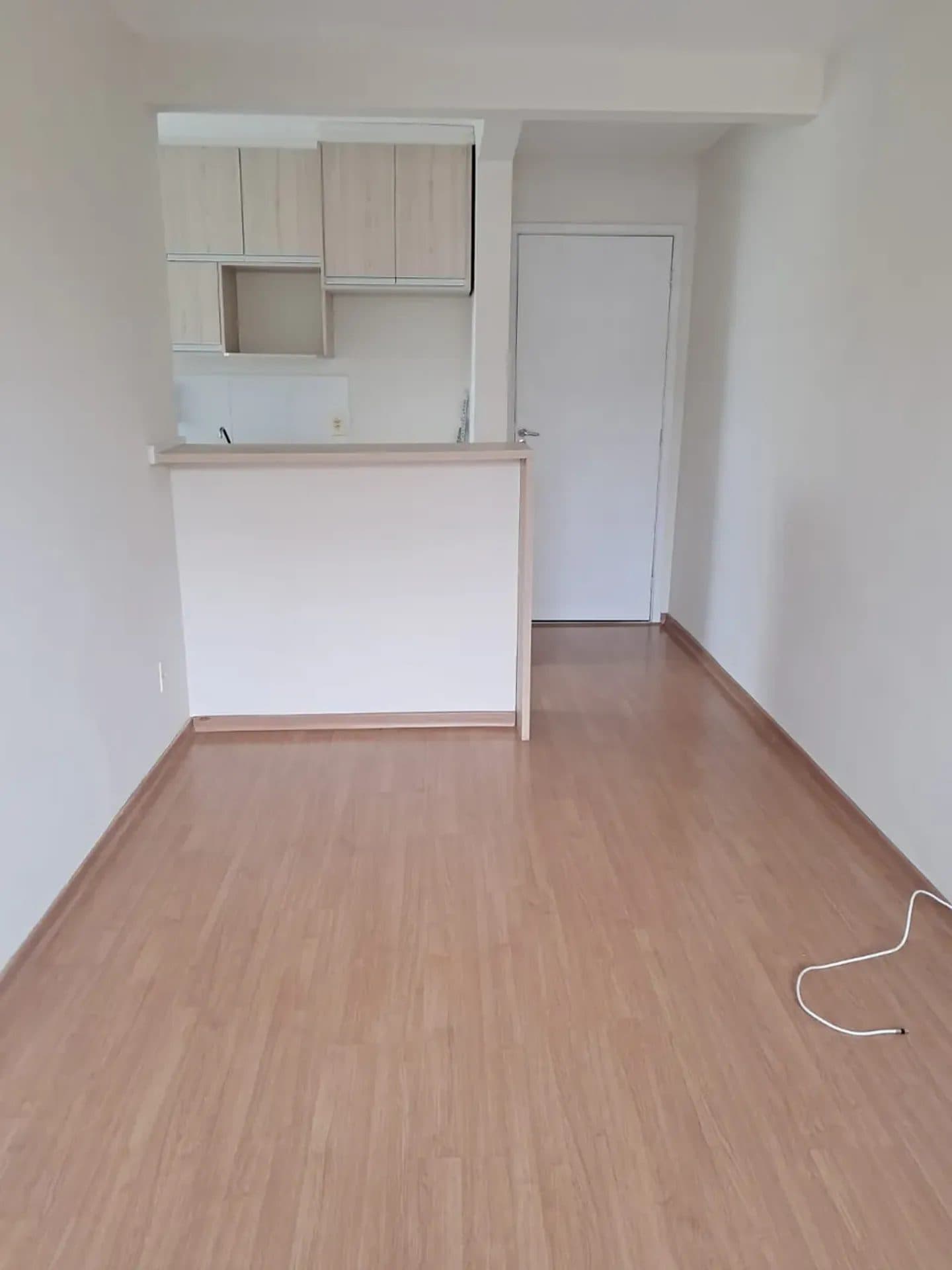 Sala de estar com piso amadeirado e passagem para a cozinha.