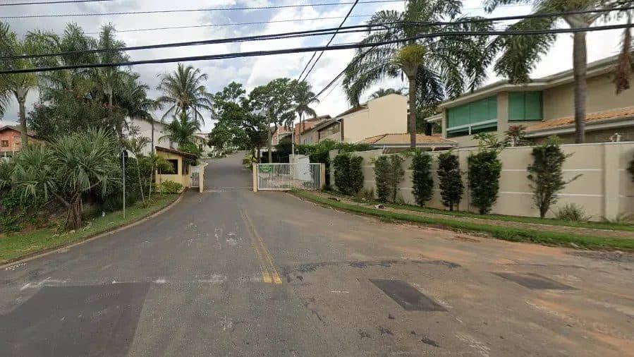Vista da rua de acesso ao condomínio com portaria e arborização.