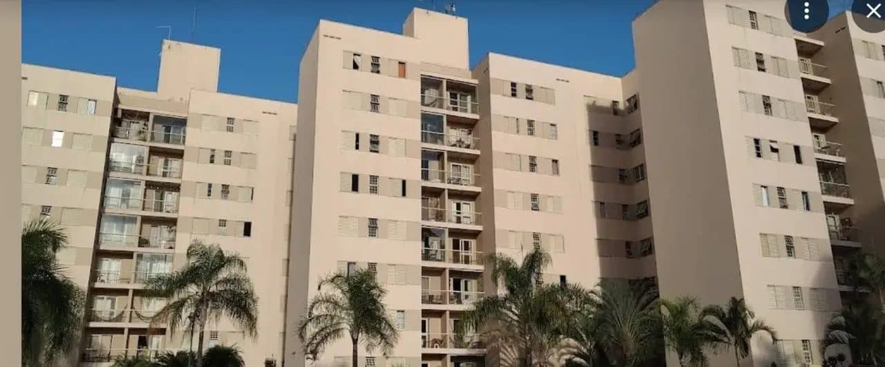 Fachada dos prédios do condomínio com varandas e palmeiras no térreo.