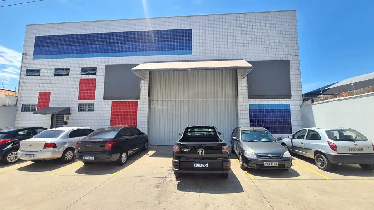 Vista frontal externa de galpão comercial com estacionamento privativo e portão de acesso para veículos.