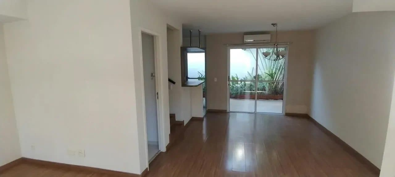 Sala de estar com piso laminado, ar-condicionado e porta de vidro com acesso a área externa.