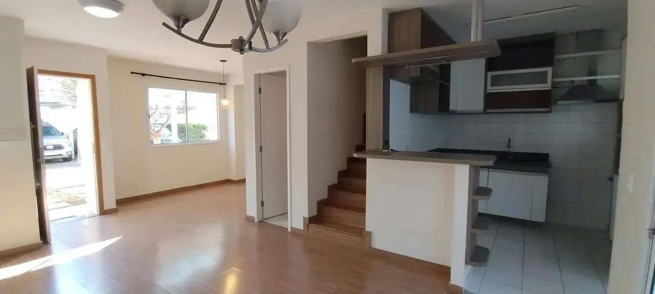 Sala de estar integrada à cozinha americana, com piso laminado e escada de acesso ao piso superior.