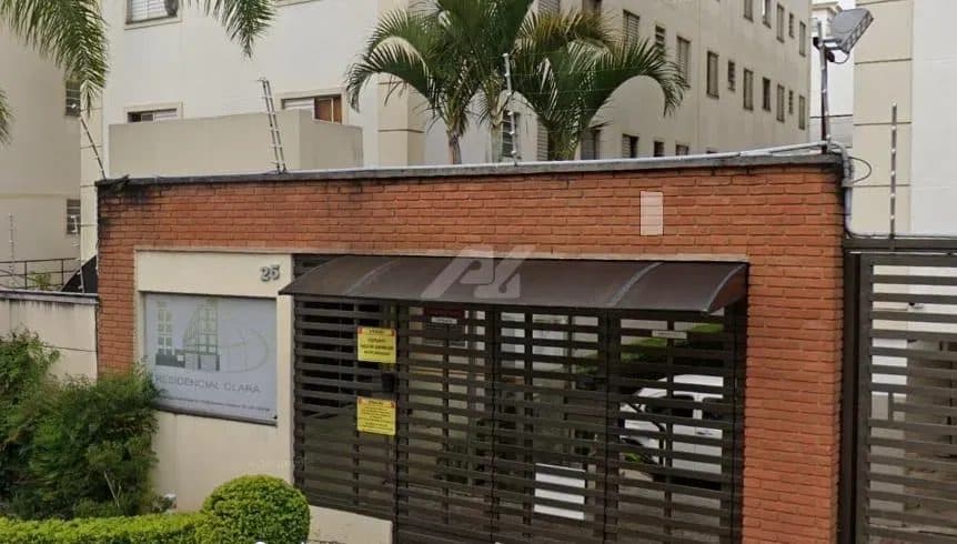 Fachada do condomínio com portão de ferro e muro de tijolos aparentes.