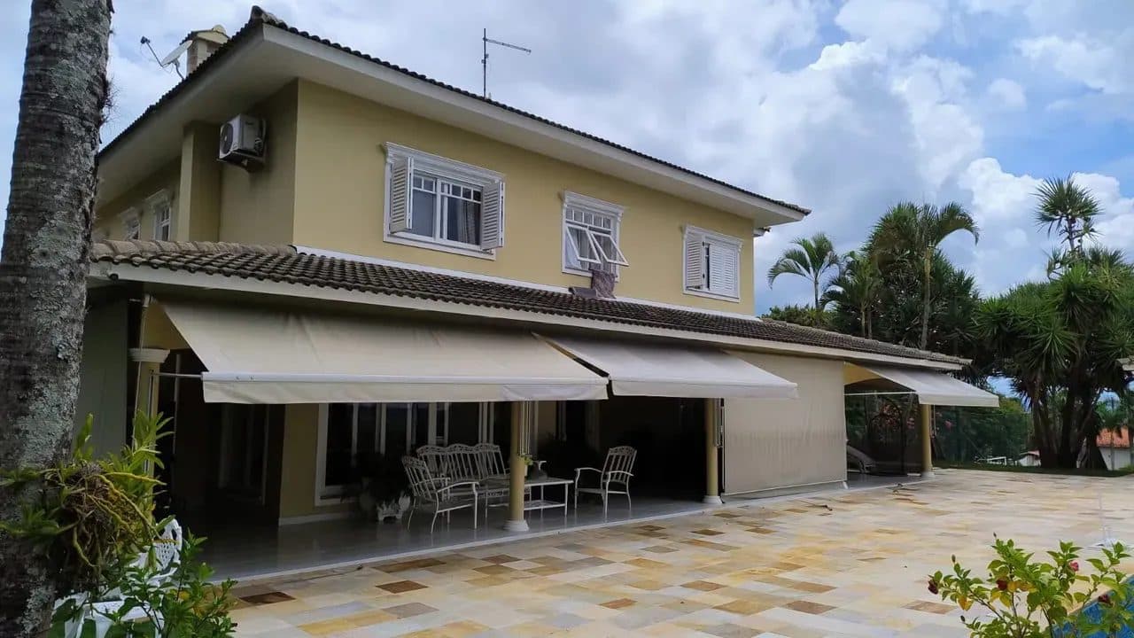 Fachada lateral de casa de dois andares com varanda coberta por toldos retráteis e piso em pedras claras.