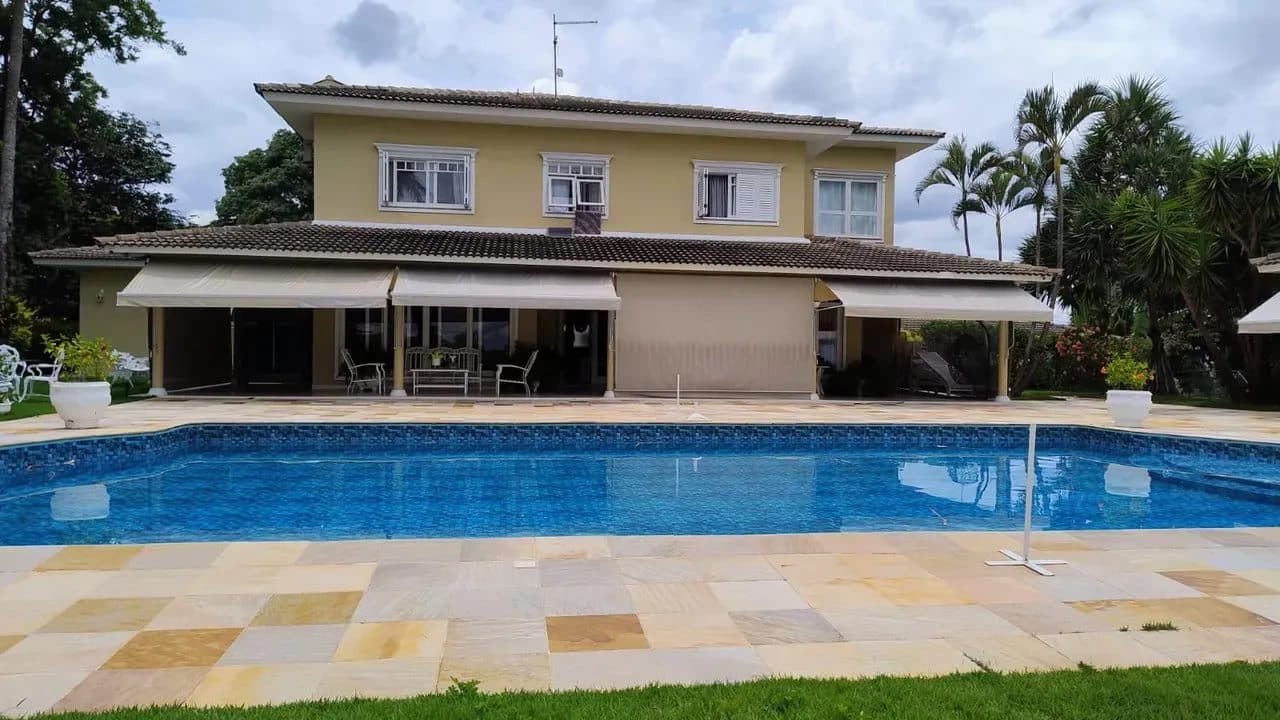 Fachada posterior de casa de dois andares com varanda, toldos retráteis e piscina em primeiro plano.
