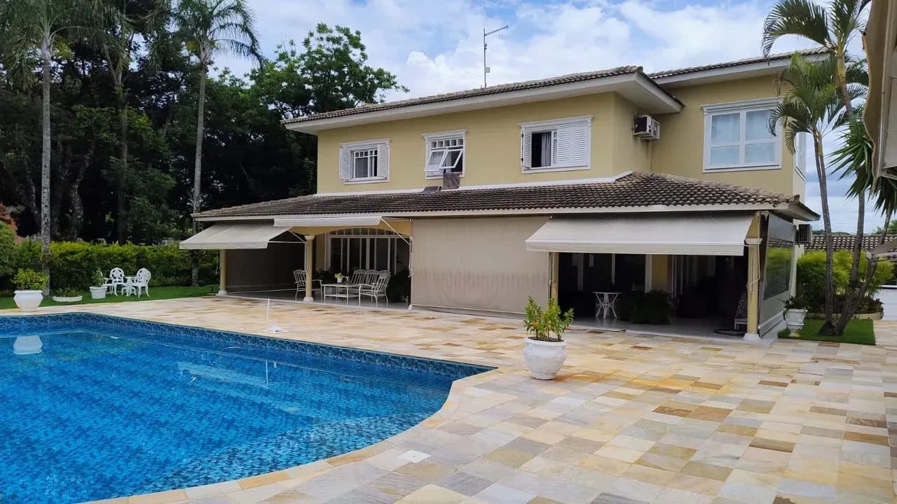 Fachada posterior de casa de dois andares com varanda, toldos retráteis e piscina com deck de pedras.